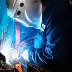 Welder welding with a Bernard GMAW gun as sparks fly