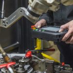 Closeup of weld cell supervisor programming robot with teach pendant